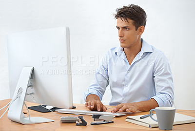 Buy stock photo A handsome young businessman sitting behind his desk working on his computer