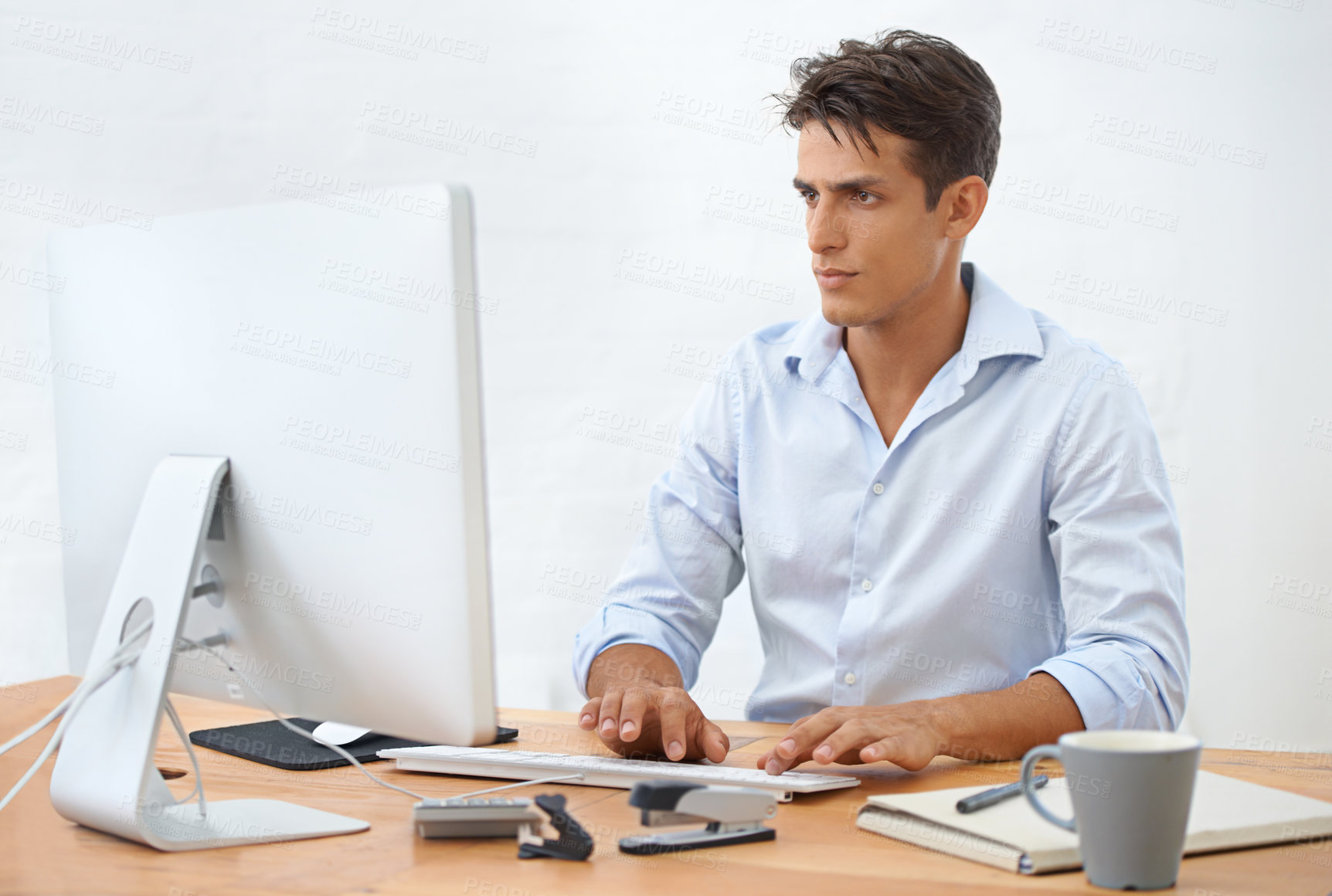 Buy stock photo A handsome young businessman sitting behind his desk working on his computer