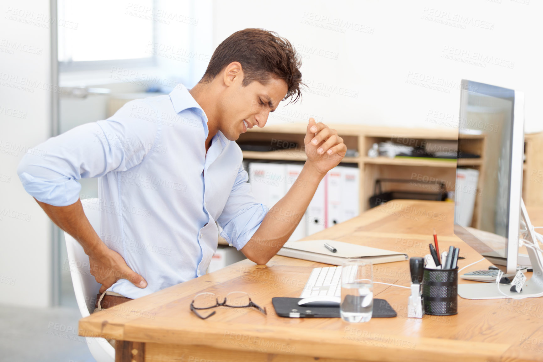 Buy stock photo Shot of a young office worker sitting at his desk with a sore back