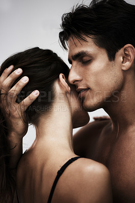 Buy stock photo Studio shot of a young couple sharing an intimate moment against a gray background