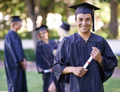 Buy stock photo Portrait of a smiling graduate holding his diploma with her former graduates in the background