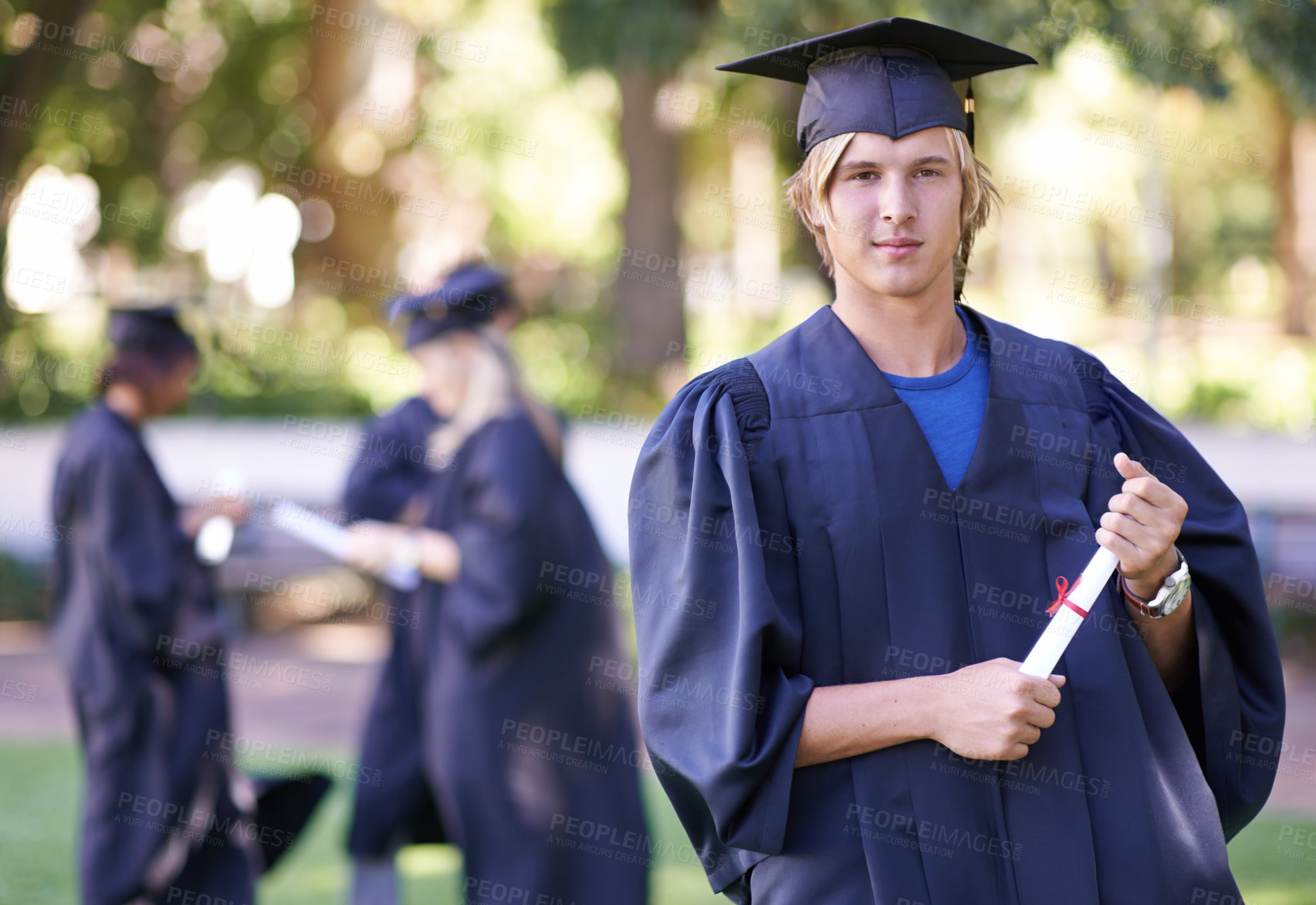 Buy stock photo Portrait of a smiling graduate holding his diploma with her former graduates in the background