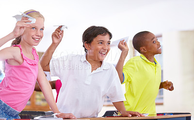 Buy stock photo Happy kids, students and paper plane in classroom on break at desk for fun games to throw or relax. Diversity, distraction or children playing with smile, origami jet or airplane in school together