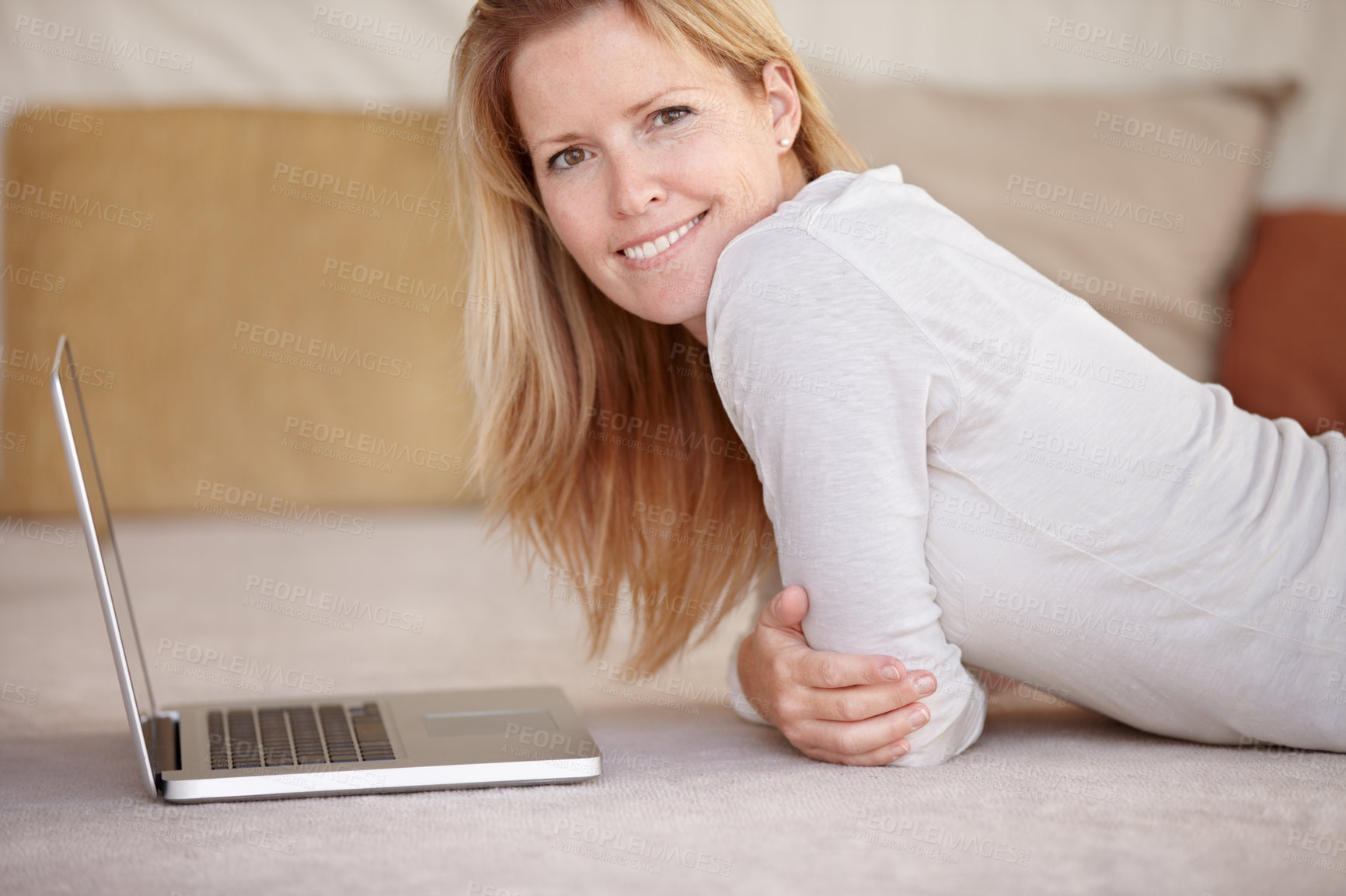 Buy stock photo A beautiful mature woman working on her laptop while lying on the floor