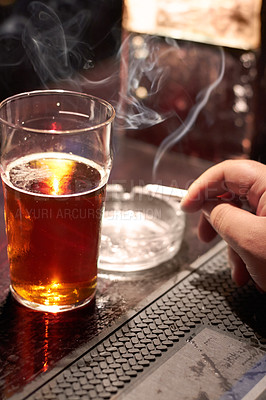 Buy stock photo Cropped shot of a man's hand holding a cigarette and a glass of beer on the counter