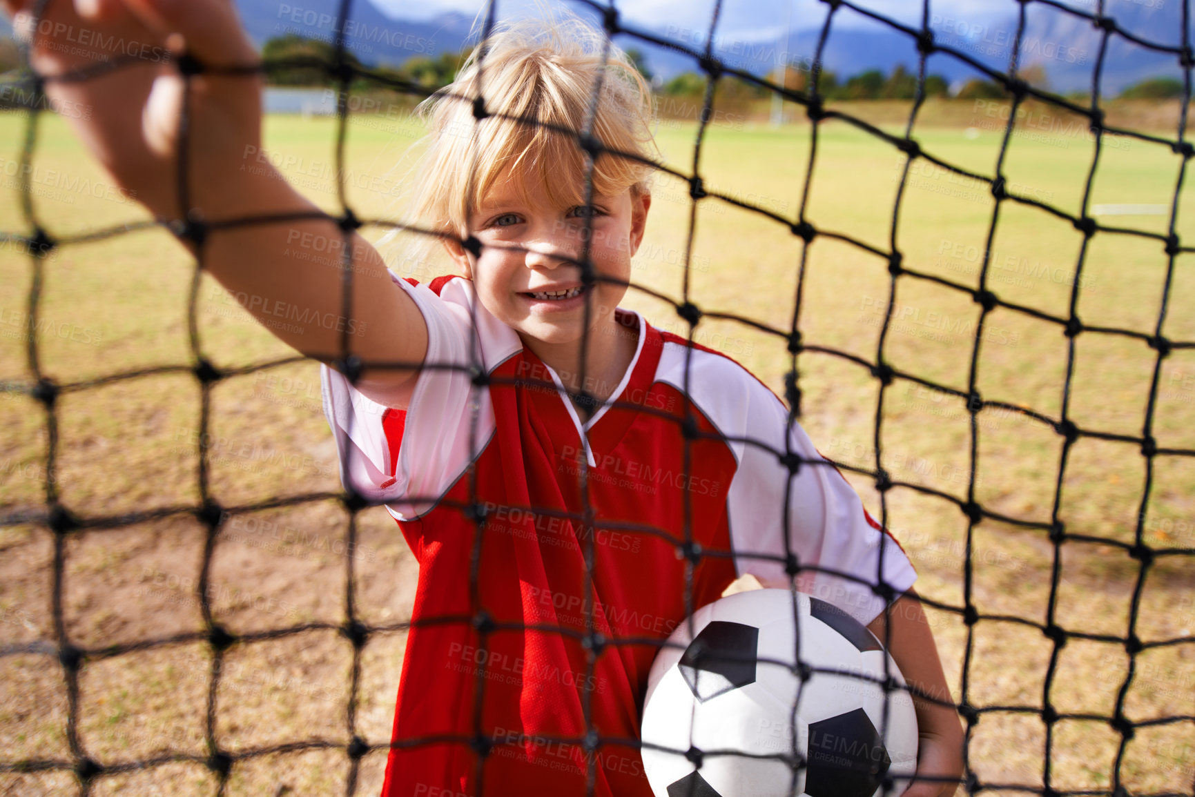 Buy stock photo Girl, soccer player and ball on goal net, smile and happy for game, field and child. Outdoor, playful and sport for childhood, portrait and athlete for match, alone and outside on football pitch