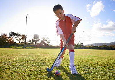 Buy stock photo Kid, ball and playing hockey on green grass for game, sports or outdoor practice match. Young child or player enjoying day on field for fitness, activity or training alone in nature with blue sky