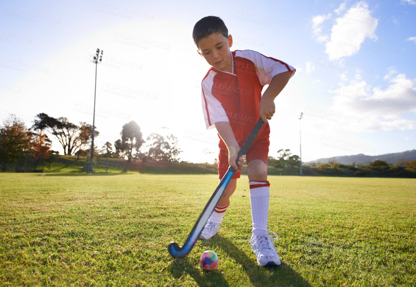 Buy stock photo Kid, ball and playing hockey on green grass for game, sports or outdoor practice match. Young child or player enjoying day on field for fitness, activity or training alone in nature with blue sky