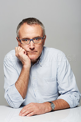 Buy stock photo Serious, portrait and senior businessman in a studio with pride for legal corporate career. Glasses, table and professional elderly male lawyer with bored face expression isolated by gray background.