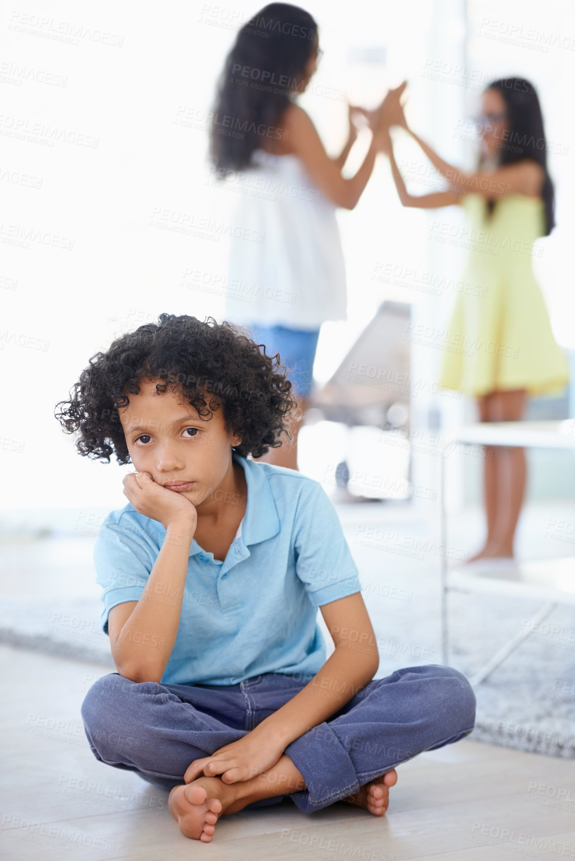 Buy stock photo Portrait of a sad-looking little boy sitting along with his sisters playing in the background