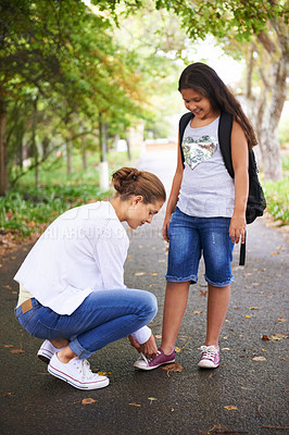 Buy stock photo Woman, teacher and tying student shoes in park for back to school, learning or education in nature. Female person teaching little girl to tie laces on asphalt path, road or outdoor street in woods