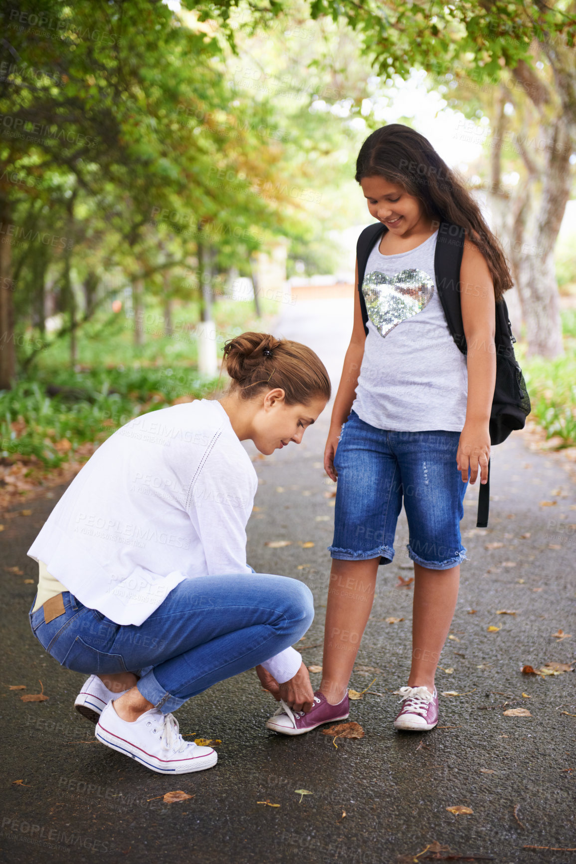 Buy stock photo Woman, teacher and tying student shoes in park for back to school, learning or education in nature. Female person teaching little girl to tie laces on asphalt path, road or outdoor street in woods