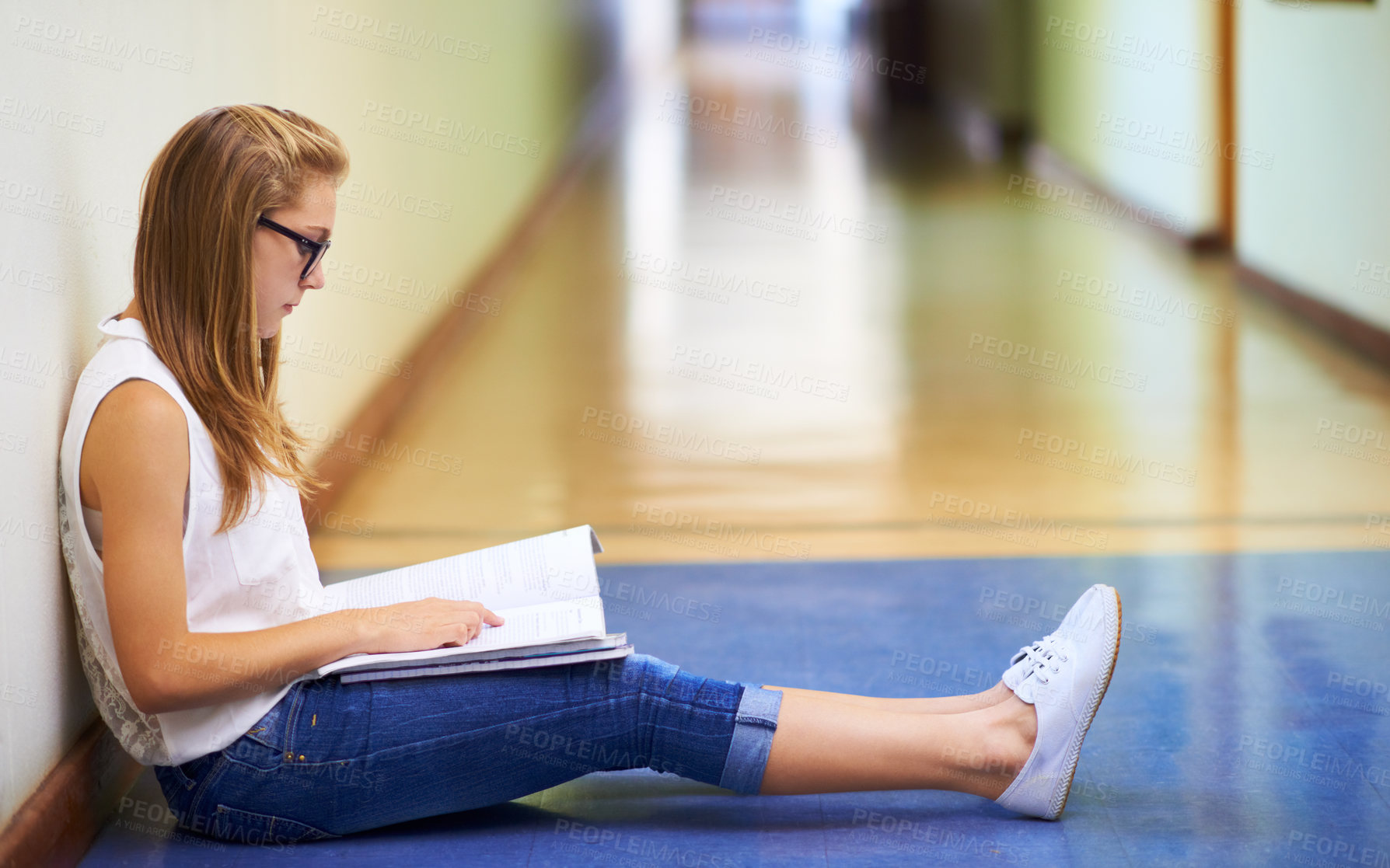 Buy stock photo Woman, teenager and student reading book in hallway at school for learning, education or studying. Female person or young child or kid sitting on floor in corridor with textbook outside classroom
