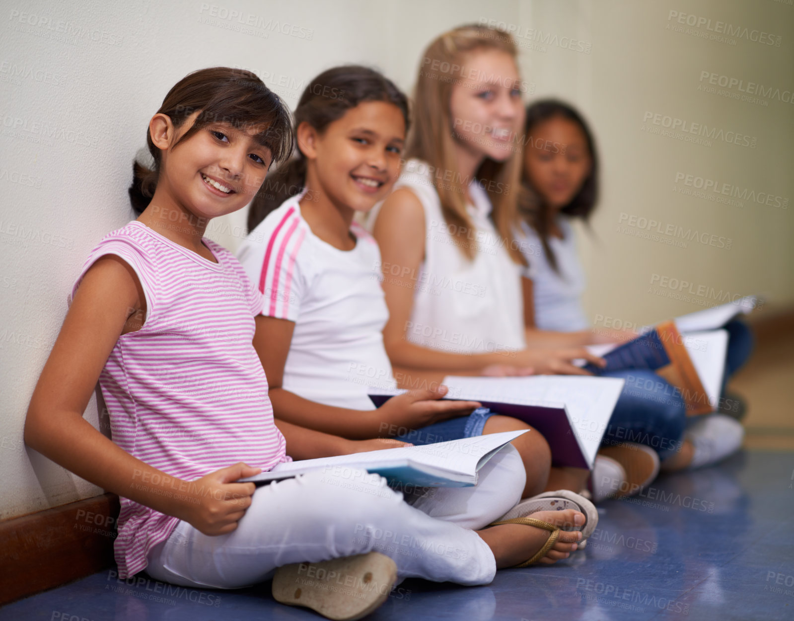Buy stock photo Girl, students and portrait of friends with books sitting at school in hallway for education or learning. Group of young kids or children smile with textbooks on corridor floor outside classroom