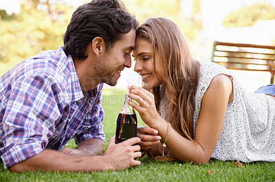Buy stock photo Nature, love and couple sharing a drink while on a summer picnic date in an outdoor garden. Happy, smile and young man and woman drinking a bottle of cola together while relaxing on grass in a field.