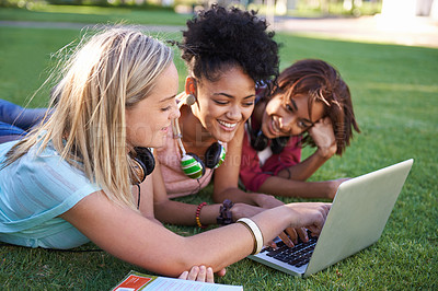 Buy stock photo Three young students lying on the grass in a park and using a laptop