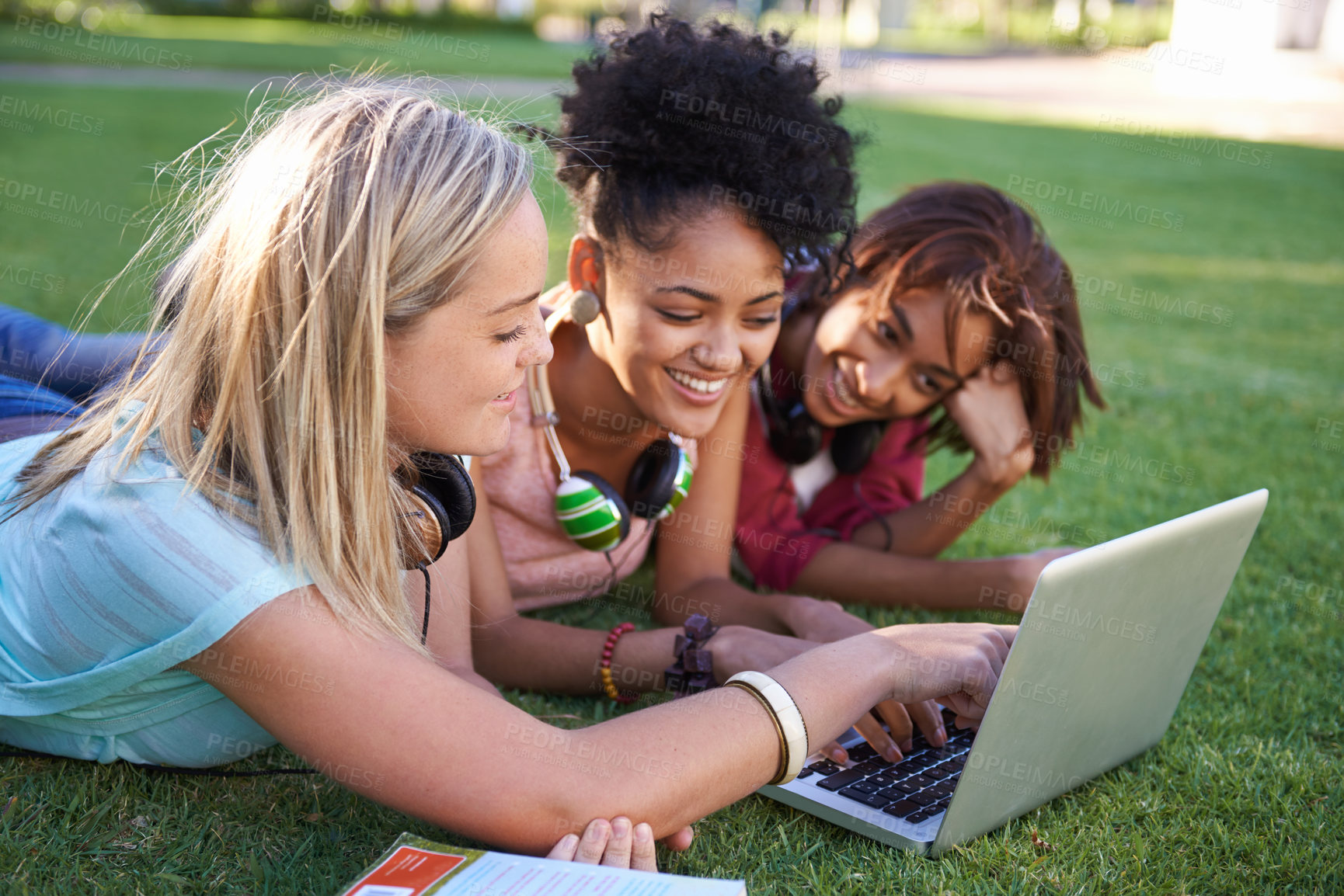 Buy stock photo Three young students lying on the grass in a park and using a laptop