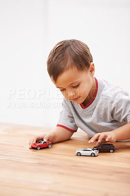 Buy stock photo Cars, toys and boy child by table playing for learning, development and fun at modern home. Cute, sweet and young kid enjoying a game with plastic vehicles by wood for childhood hobby at house.