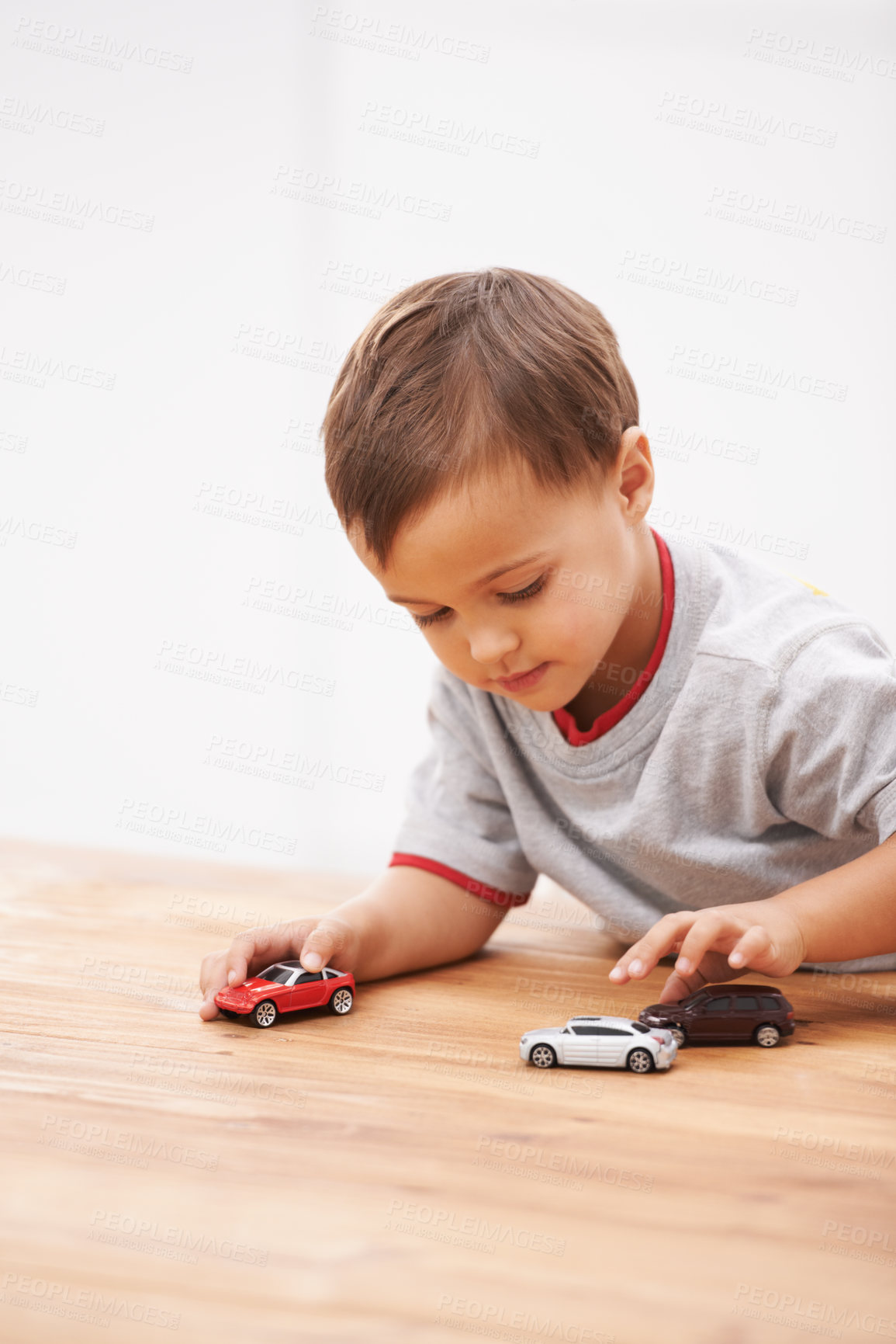 Buy stock photo Cars, toys and boy child by table playing for learning, development and fun at modern home. Cute, sweet and young kid enjoying a game with plastic vehicles by wood for childhood hobby at house.