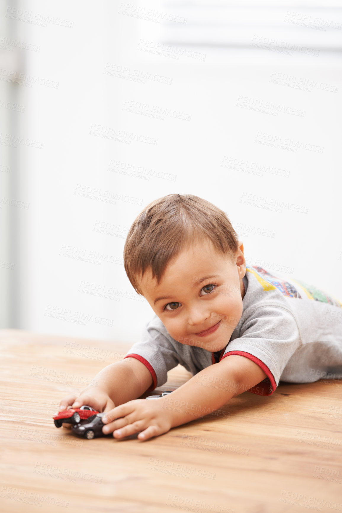 Buy stock photo Cars, toys and portrait of child by table playing for learning, development and fun at modern home. Cute, sweet and boy kid enjoying a game with plastic vehicles by wood for childhood hobby at house.