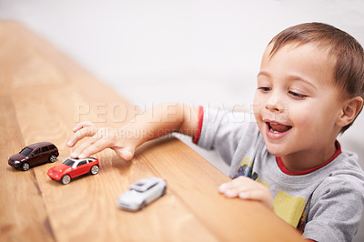 Buy stock photo Cars, toys and boy kid by table playing for learning, development and fun at modern home. Cute, sweet and young child enjoying a game with plastic vehicles by wood for childhood hobby at house.