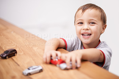 Buy stock photo Cars, toys and boy kid by table playing for learning, development and fun at modern home. Cute, sweet and portrait of child enjoying a game with plastic vehicles by wood for childhood hobby at house.