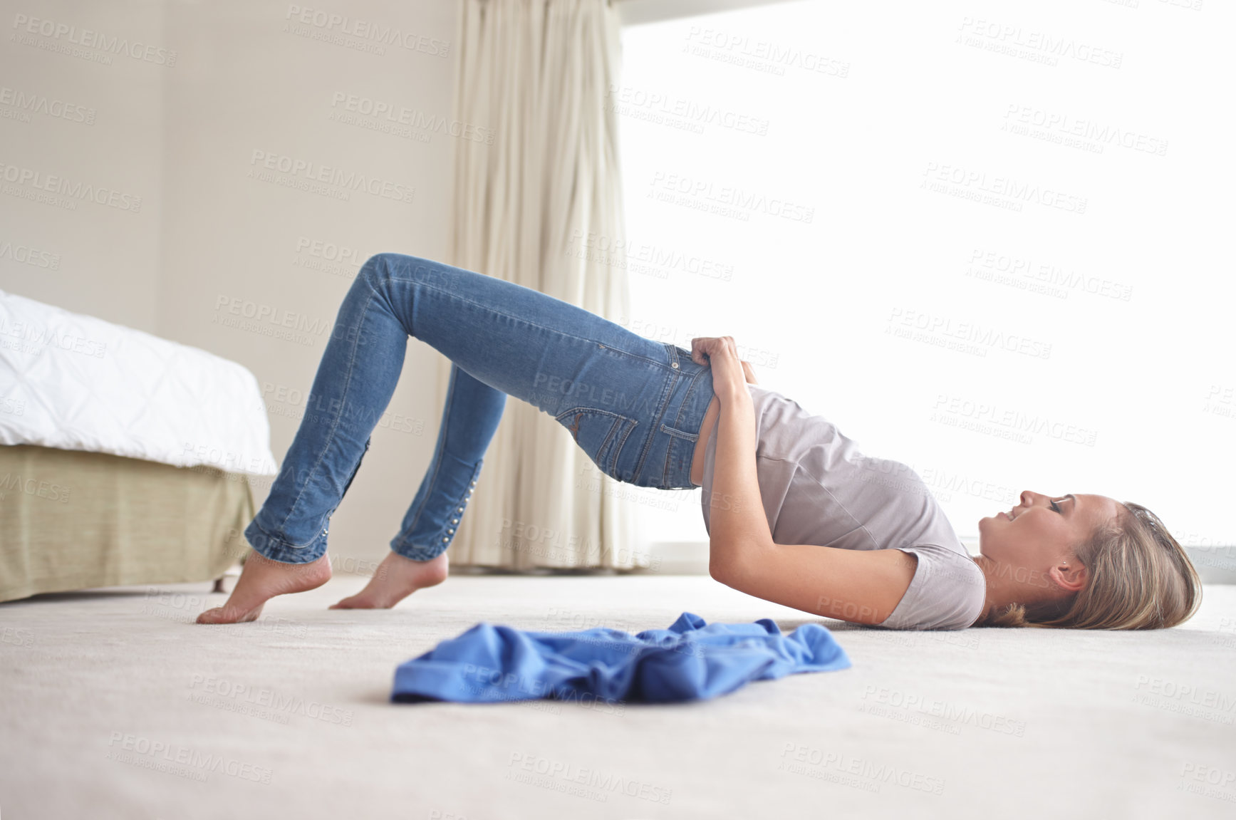 Buy stock photo A young woman struggling to pull on her jeans