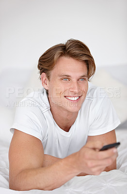 Buy stock photo A handsome young man wearing his pjamas and watching tv while sitting in bed