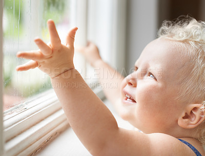 Buy stock photo Baby, rain and happy child by window, curious and smile alone with wet weather. Young kid, glass and dream of blonde toddler thinking of childhood, cute girl playing and watch for learning at house