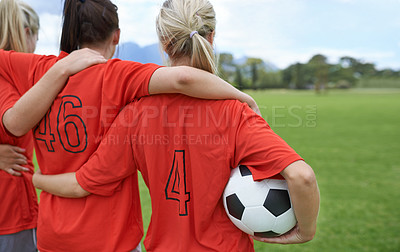 Buy stock photo A girls soccer team standing with their arms around each other's shoulders looking towards the field