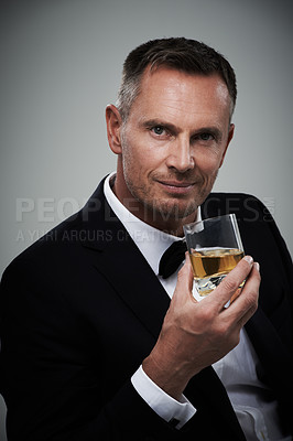Buy stock photo Portrait, whiskey and elegant with a man model in studio on a gray background drinking an alcoholic beverage. Gentleman, whisky and tuxedo with a handsome mature man enjoying a drink of alcohol