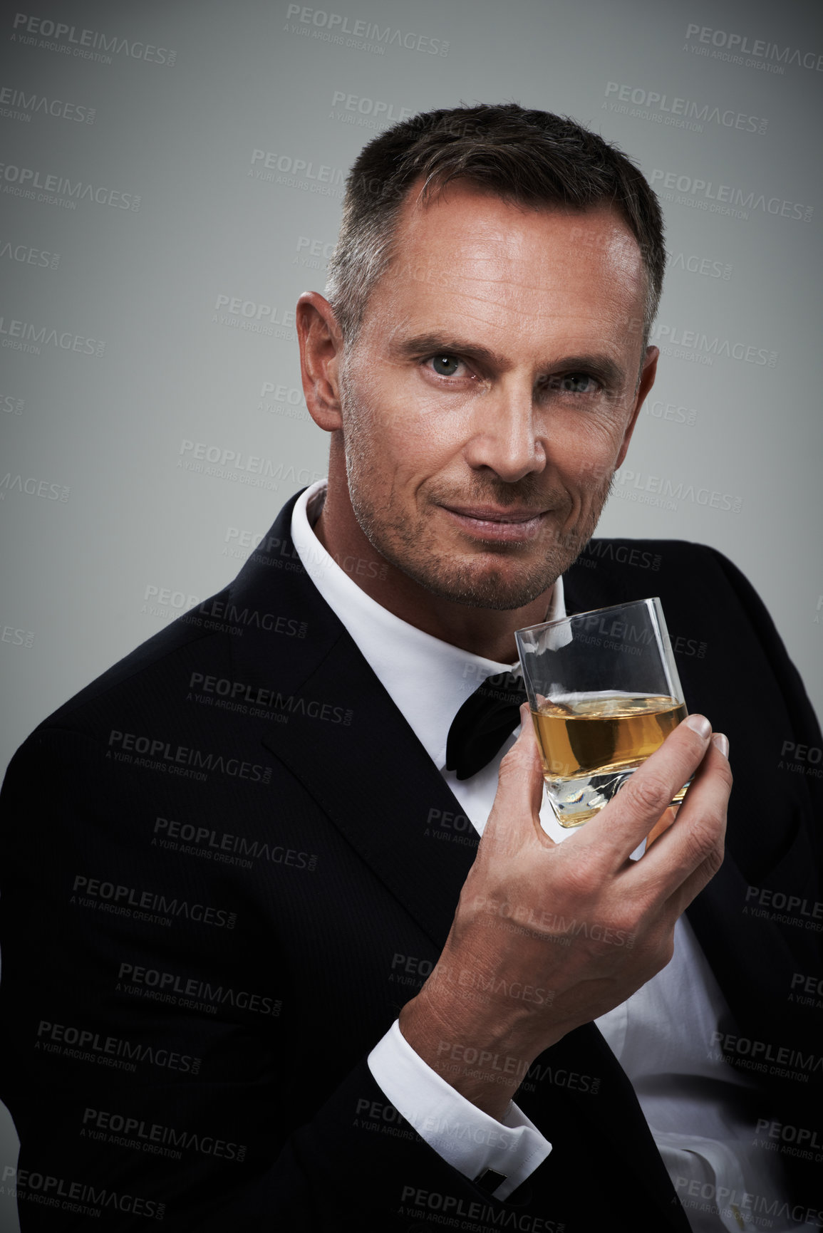 Buy stock photo Portrait, whiskey and elegant with a man model in studio on a gray background drinking an alcoholic beverage. Gentleman, whisky and tuxedo with a handsome mature man enjoying a drink of alcohol