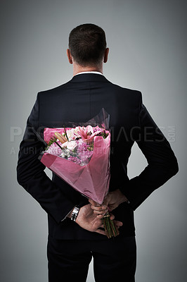Buy stock photo Valentines day, surprise and flowers of a man in a suit with love present behind back. Flower gift, suit and male model in a isolated gray background studio feeling romantic for a formal date