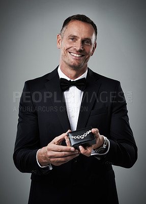 Buy stock photo Jewelry, man and portrait of a model with a smile and valentines present in a studio. Isolated, gray background and person in a suit with happiness holding a necklace gift feeling love and classy