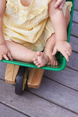 Buy stock photo Baby, child and riding toy wagon in outdoors, plastic and fun activity for childhood. Kid, toddler and wheelbarrow for playing games on porch or deck, closeup and relaxing in construction equipment