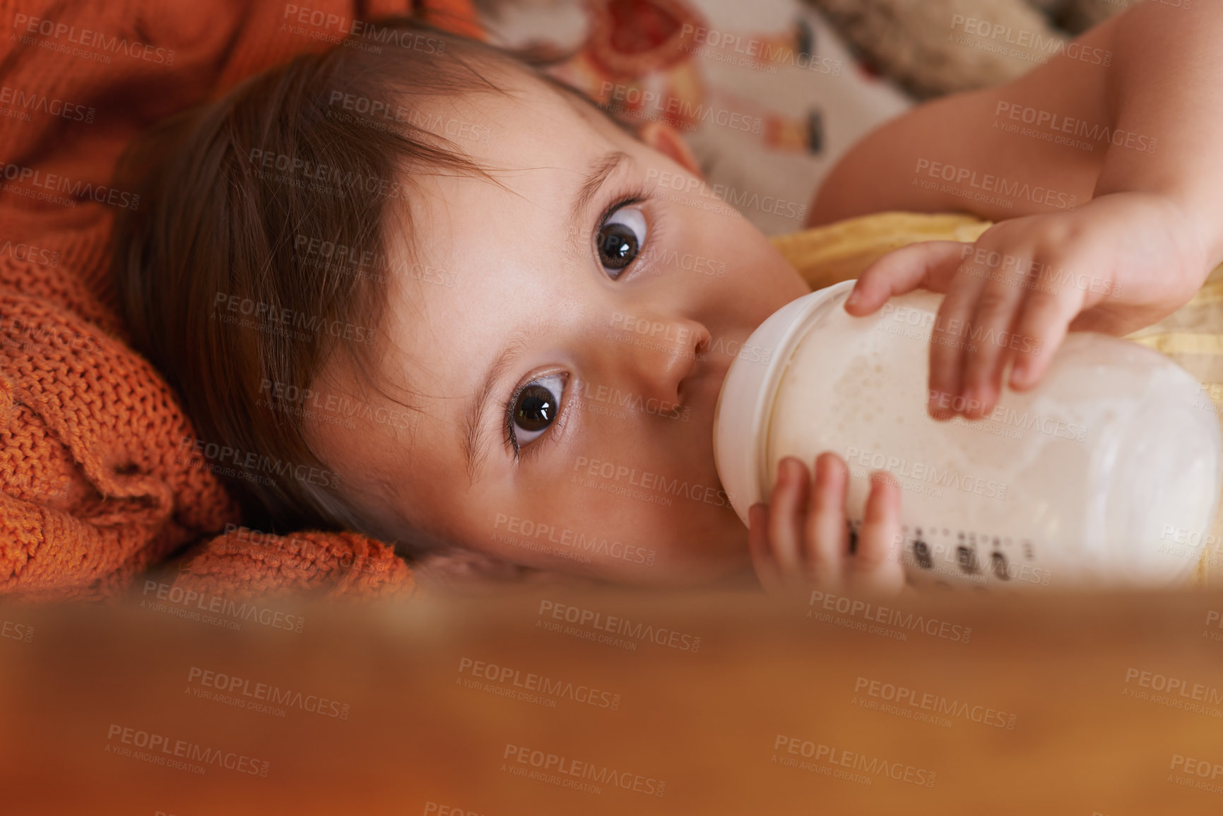 Buy stock photo A little girl looking up at the camera while drinking from her bottle