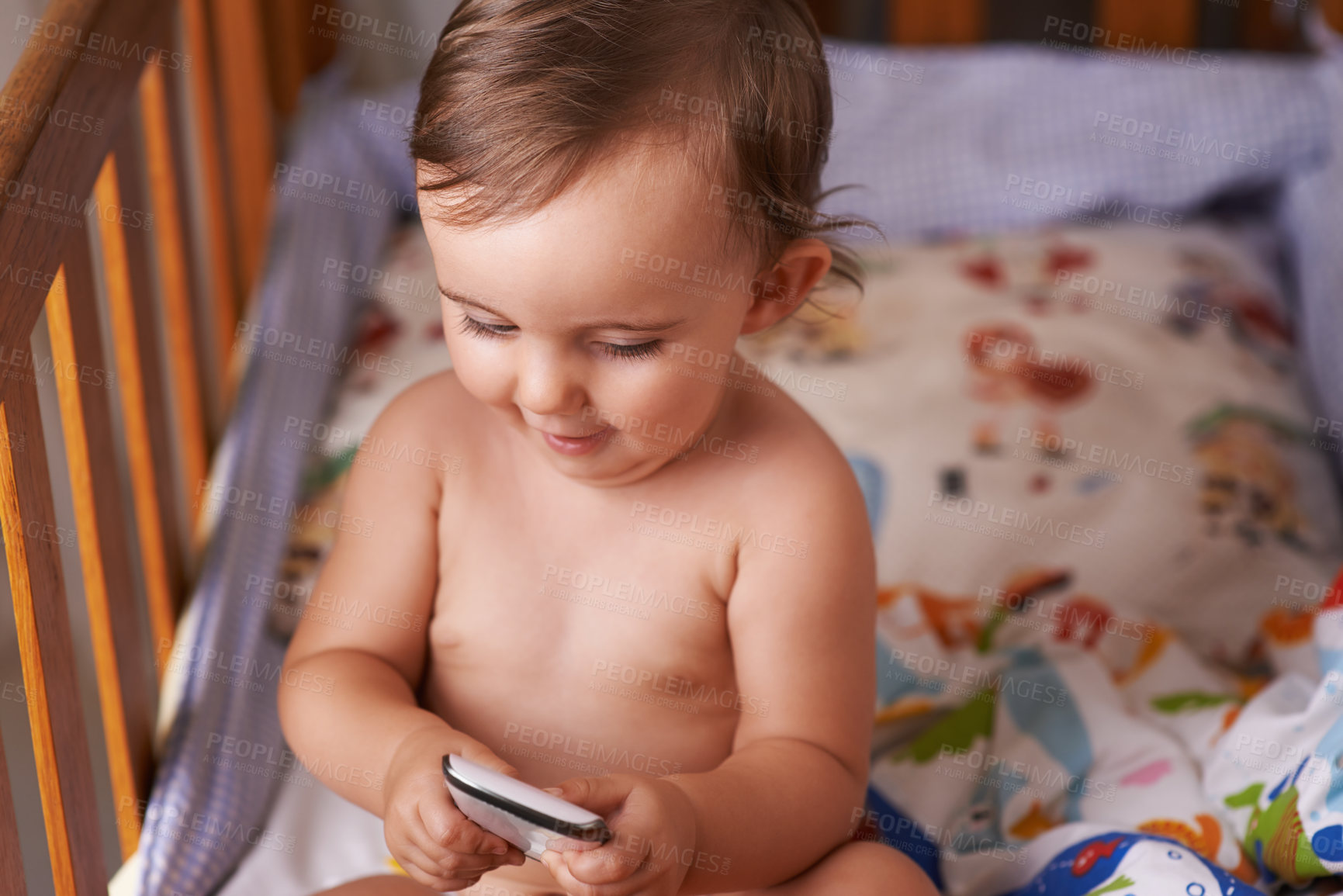 Buy stock photo A little girl sitting in her crib playing with her cellphone