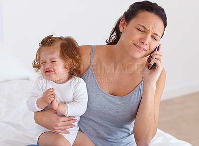 Buy stock photo A mother trying to have a phone conversation while her baby is crying in the background