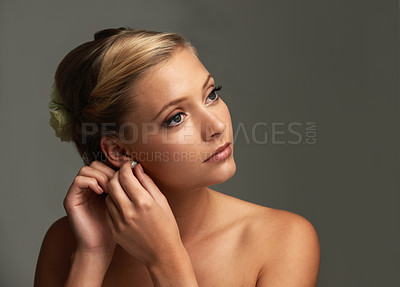 Buy stock photo Studio shot of a beautiful young woman putting earrings onl