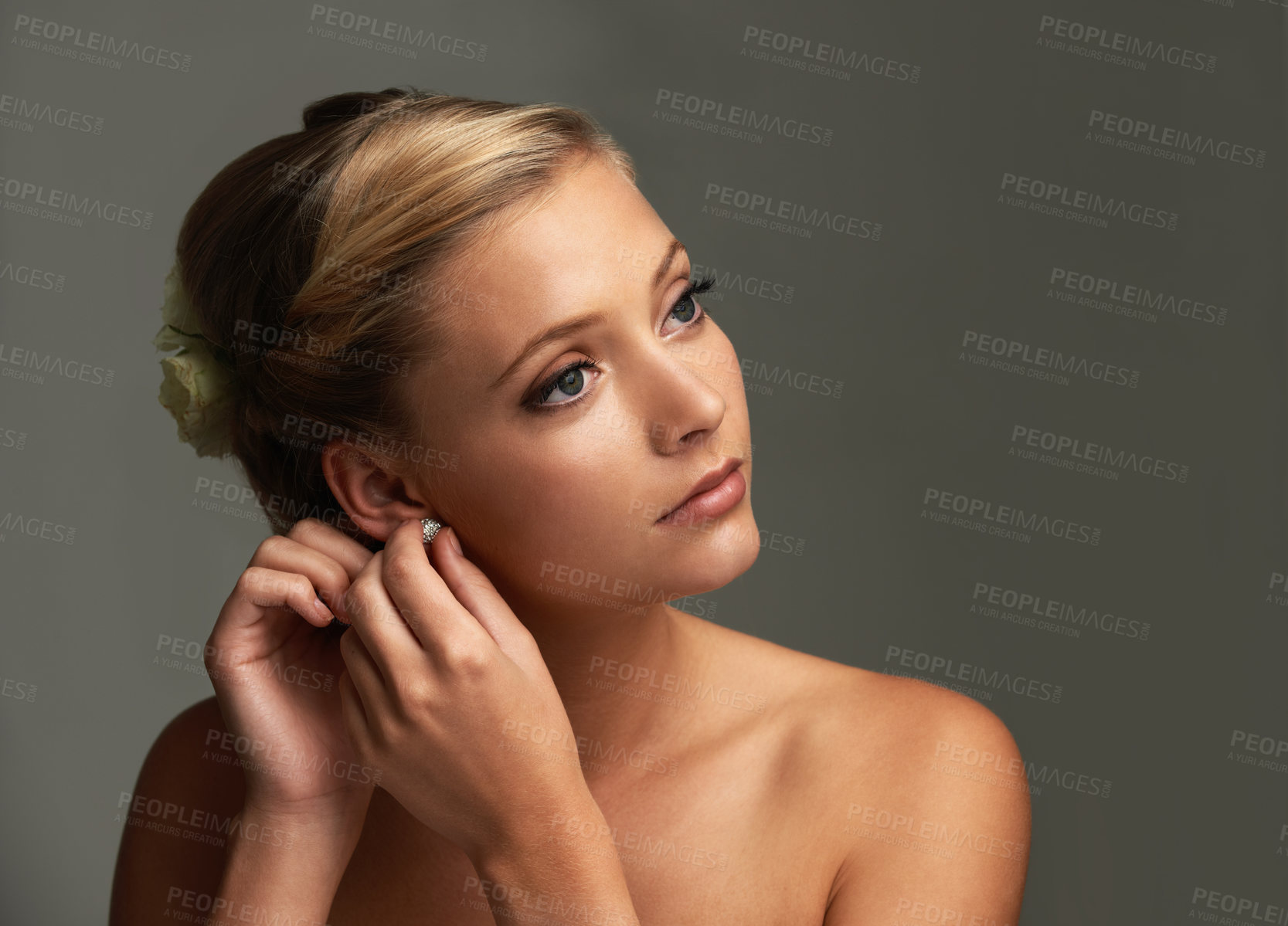 Buy stock photo Studio shot of a beautiful young woman putting earrings onl