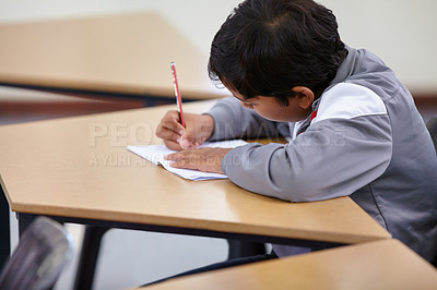 Buy stock photo Boy, school and writing in classroom with notebook, studying lesson and learning knowledge at desk. Child, student and kid drawing on paper for academic development, educational test and assessment