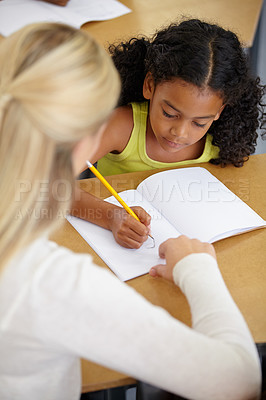Buy stock photo Teacher help child, education and writing in notebook with pencil, teaching and learning for growth and development. People in classroom to learn, academic study with young girl and woman at school