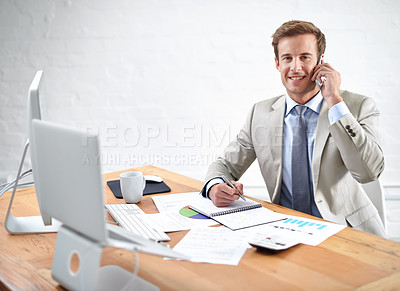 Buy stock photo Portrait of a young businessman talking on the phone while writing at his desk
