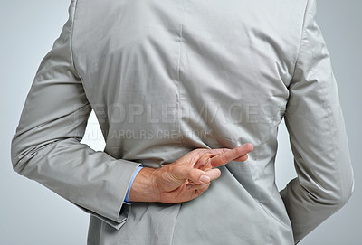 Buy stock photo Businessman, back and fingers crossed for dishonesty in studio, scam and lying or corrupt professional. Male person, fraud and cheat emoji or liar by gray background, hidden and guilty of crime