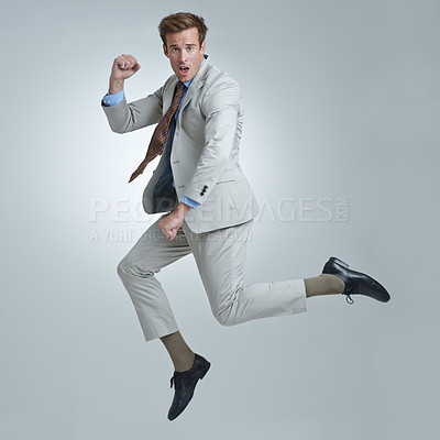 Buy stock photo Businessman, celebration and jumping for success in portrait, studio and fist pump for triumph. Male person, professional and victory or accomplishment, cheering and energy or win by gray background
