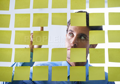 Buy stock photo Creative man, face and thinking, pointing to sticky note in schedule brainstorming or planning tasks on glass board. Thoughtful male contemplating business startup or strategy in wonder at the office