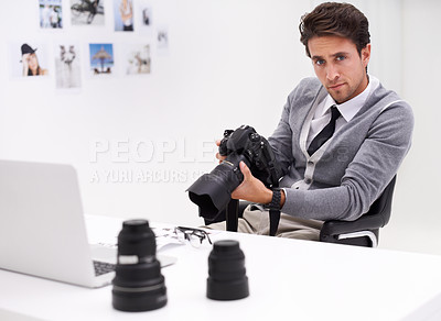 Buy stock photo Portrait of a photographer sitting at a desk in his office holding a camera