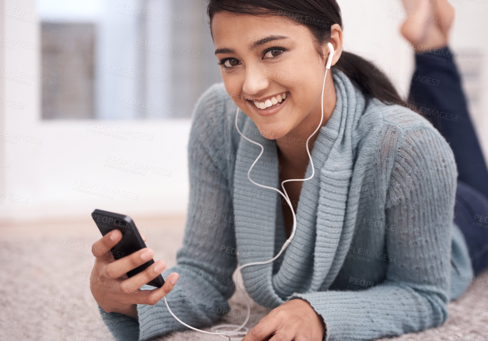 Buy stock photo Portrait of happy woman on carpet with phone, headphones and relax with mobile app for podcast in house. Face of girl lying on floor with smile, music and streaming service for online radio in home.