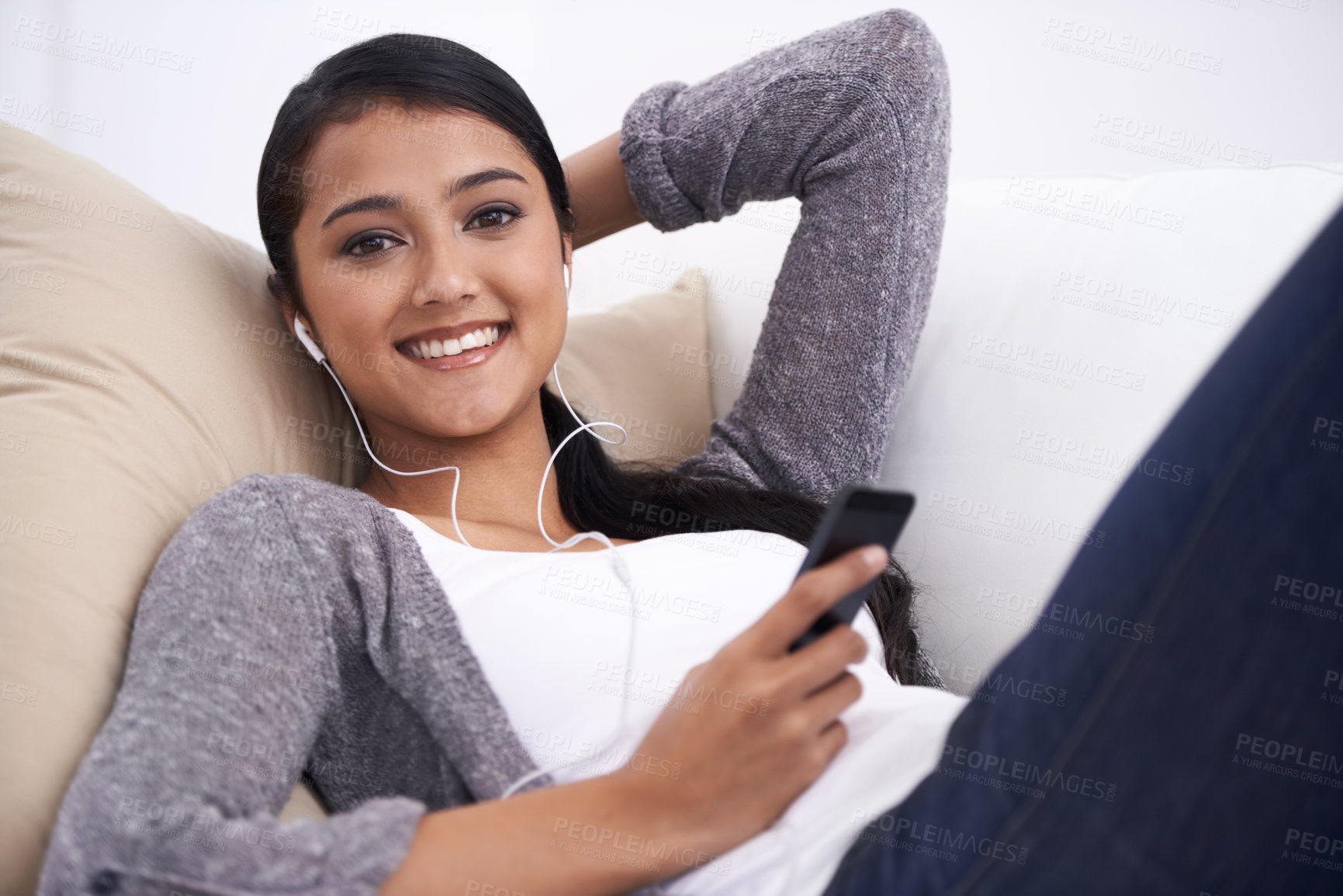 Buy stock photo Young woman, phone and earphones, relax on couch with social media, communication and music in portrait. Listen to radio, podcast or watch video online, web or blog with mobile app and tech at home