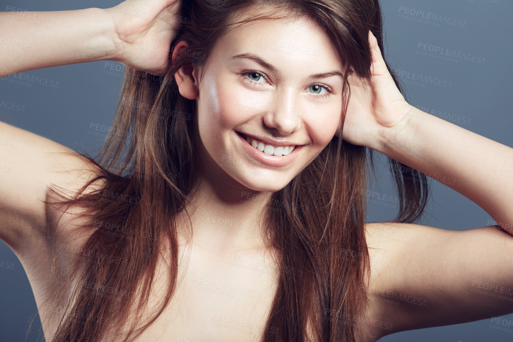 Buy stock photo Face, smile and beauty portrait of a woman in studio with natural makeup, hands in hair care and cosmetics. Headshot of aesthetic female model on a blue background for glow, skincare or facial health